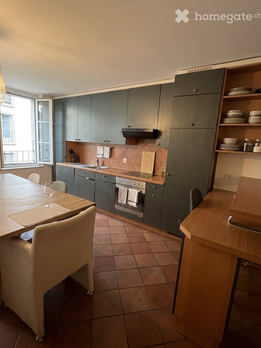 Modern kitchen with grey cabinets, stainless steel appliances, a wooden dining table with chairs, and a wine glass on the table.