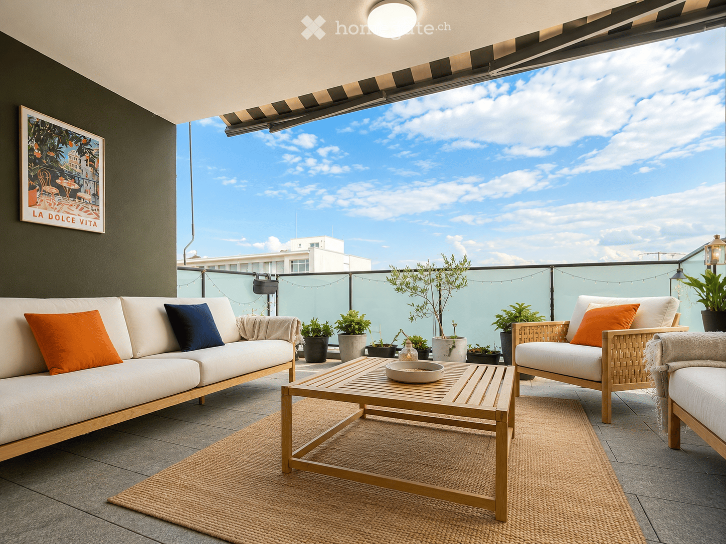 Balcony with a white sofa, wooden coffee table, wicker chair, potted plants, and a view of the sky.