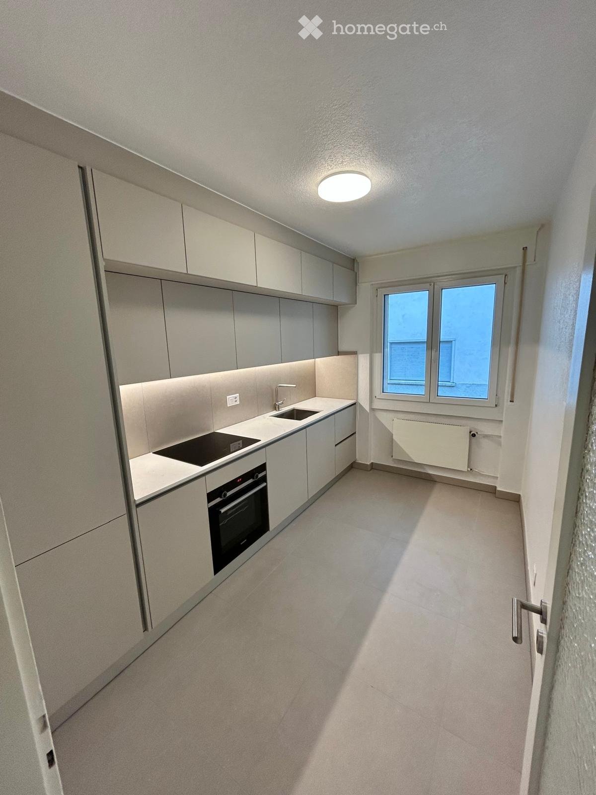 Modern kitchen with light grey cabinets, a sink, an oven, and a window providing natural light.