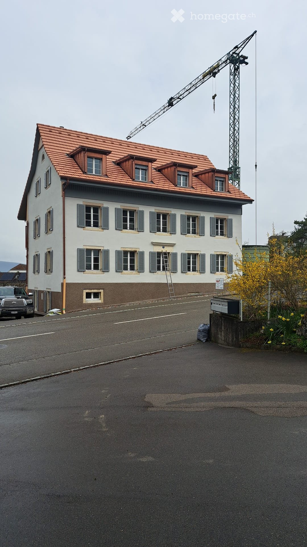 3 story house, red roof, white walls, multiple windows, brown base, crane in the background