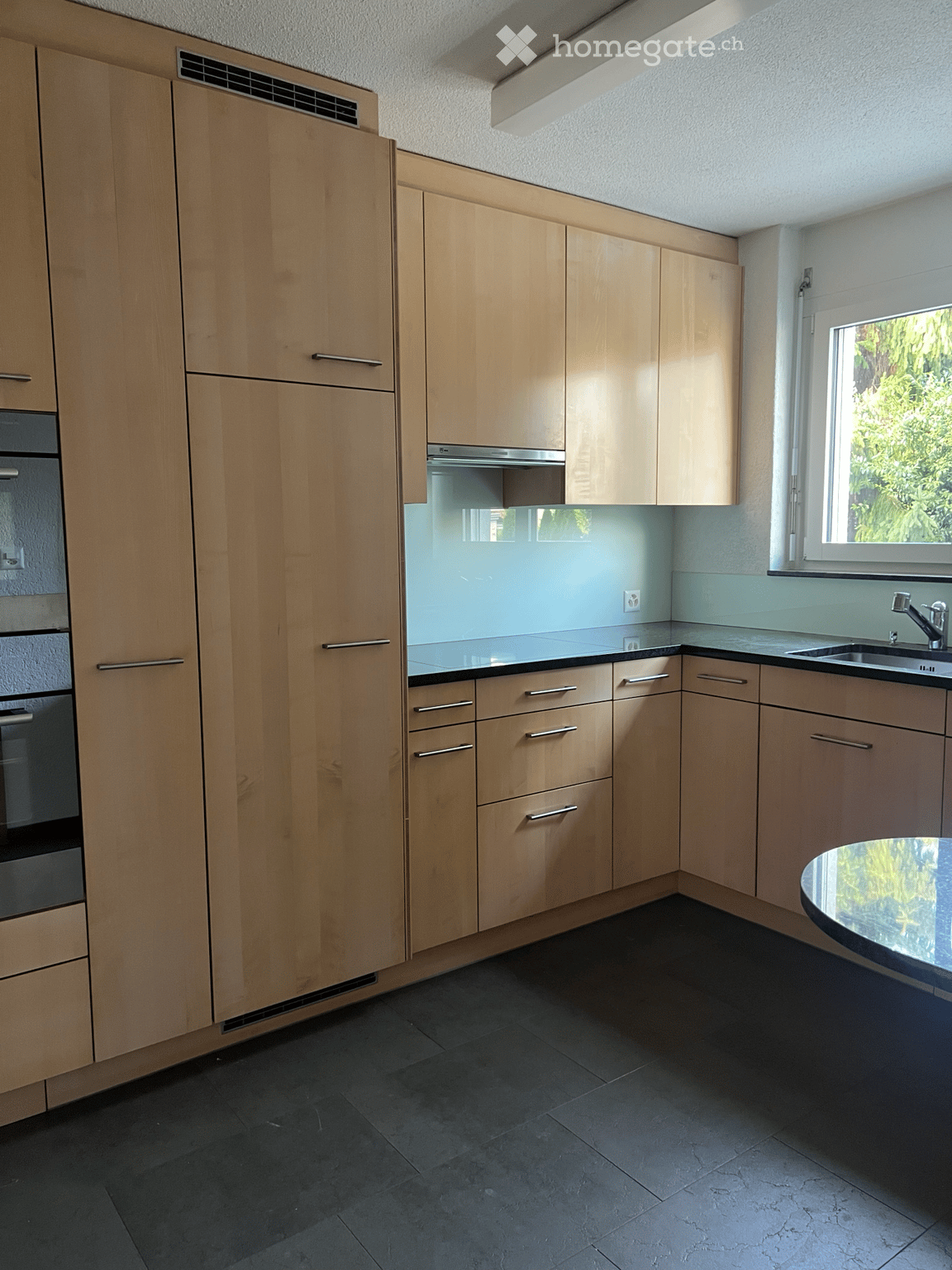 Modern kitchen with light wood cabinets, stainless steel appliances, and a black countertop.