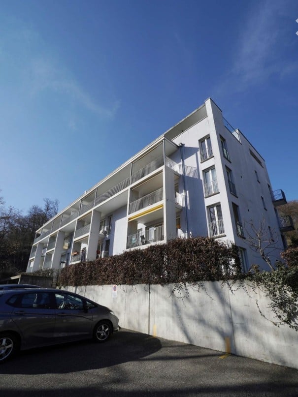 Modern multi-story apartment building with white facade, multiple balconies, and a parked car in front.