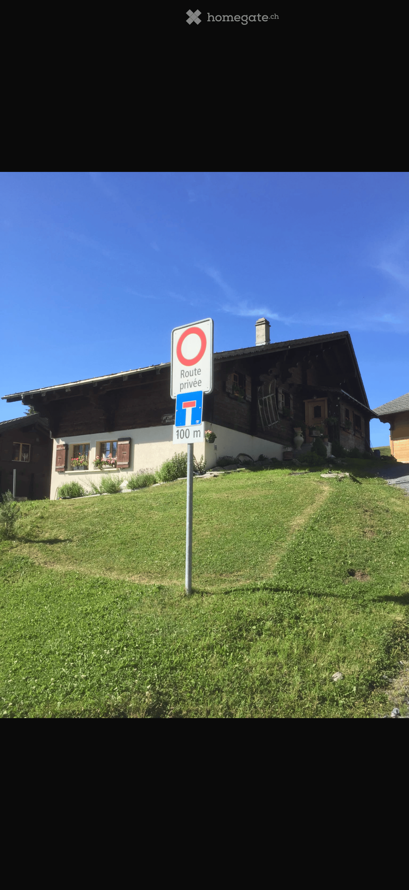 A two-story wooden house with a sloped roof, white walls, and multiple windows, surrounded by a grassy lawn and a private road sign.