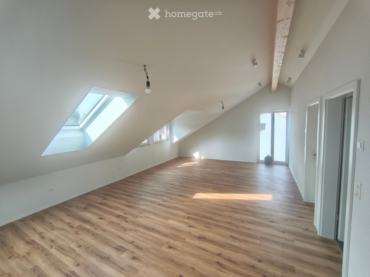 Empty attic room with wooden flooring, white walls, and skylight windows allowing natural light.