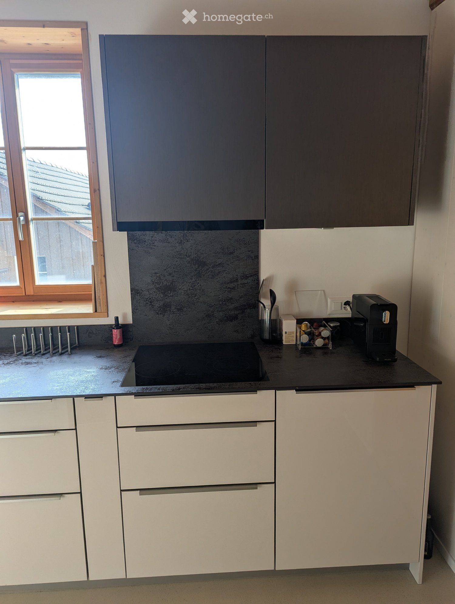 Modern kitchen with white cabinets, black countertop, induction stove, coffee maker, and various small appliances.