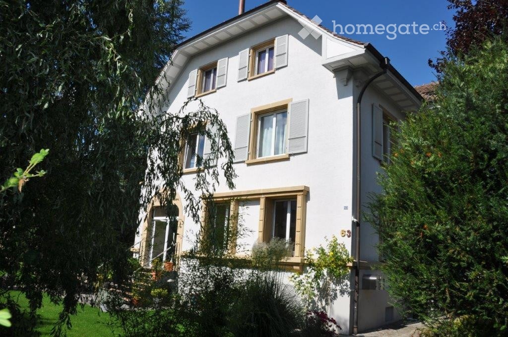 A two-story white house with multiple windows, shutters, and a well-maintained garden.