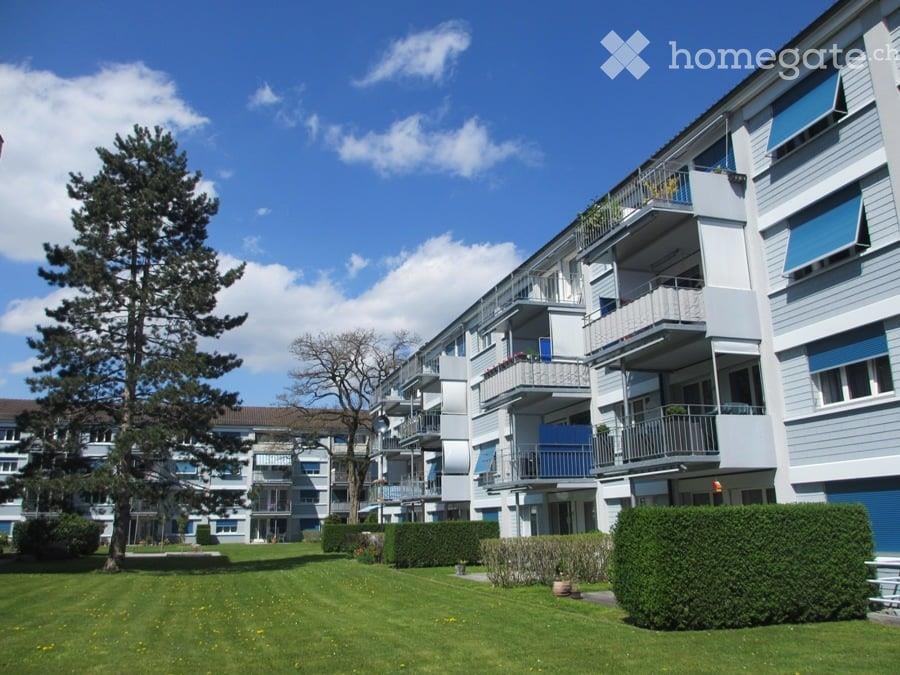 Multi-story residential building with balconies, surrounded by a well-maintained lawn and trees.