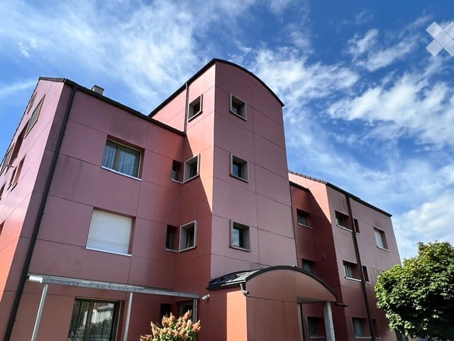 Modern multi-story residential building with pink facade, multiple windows, and a covered entrance area.