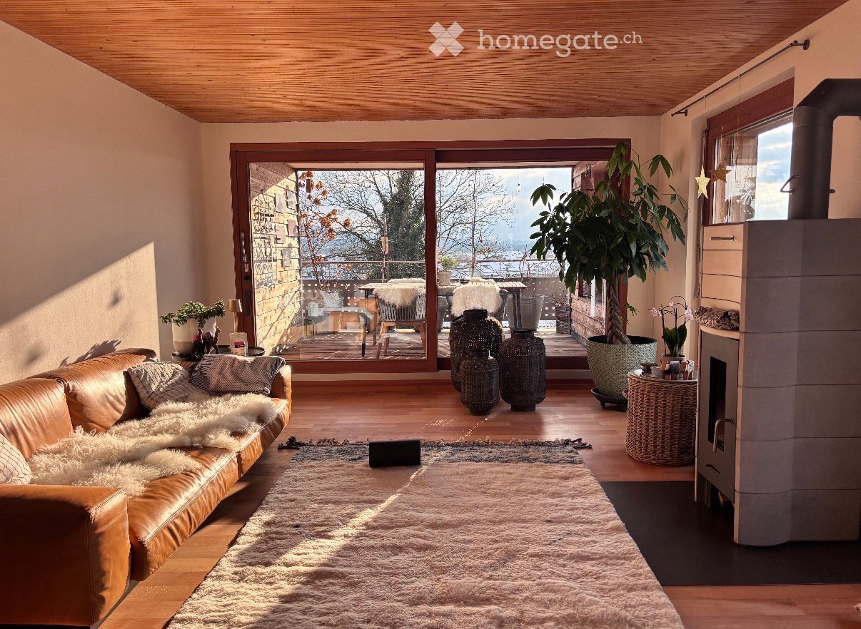 Modern living room with a leather sofa, large area rug, decorative vases, and a view of the city through large windows.