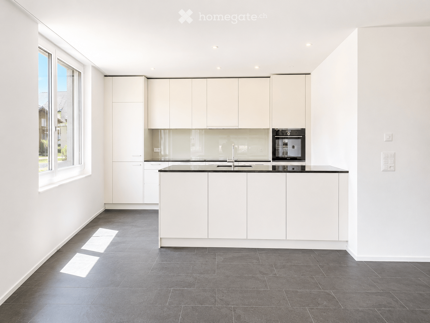 Modern kitchen with white cabinets, black countertop, and stainless steel appliances, featuring large windows and a central island.