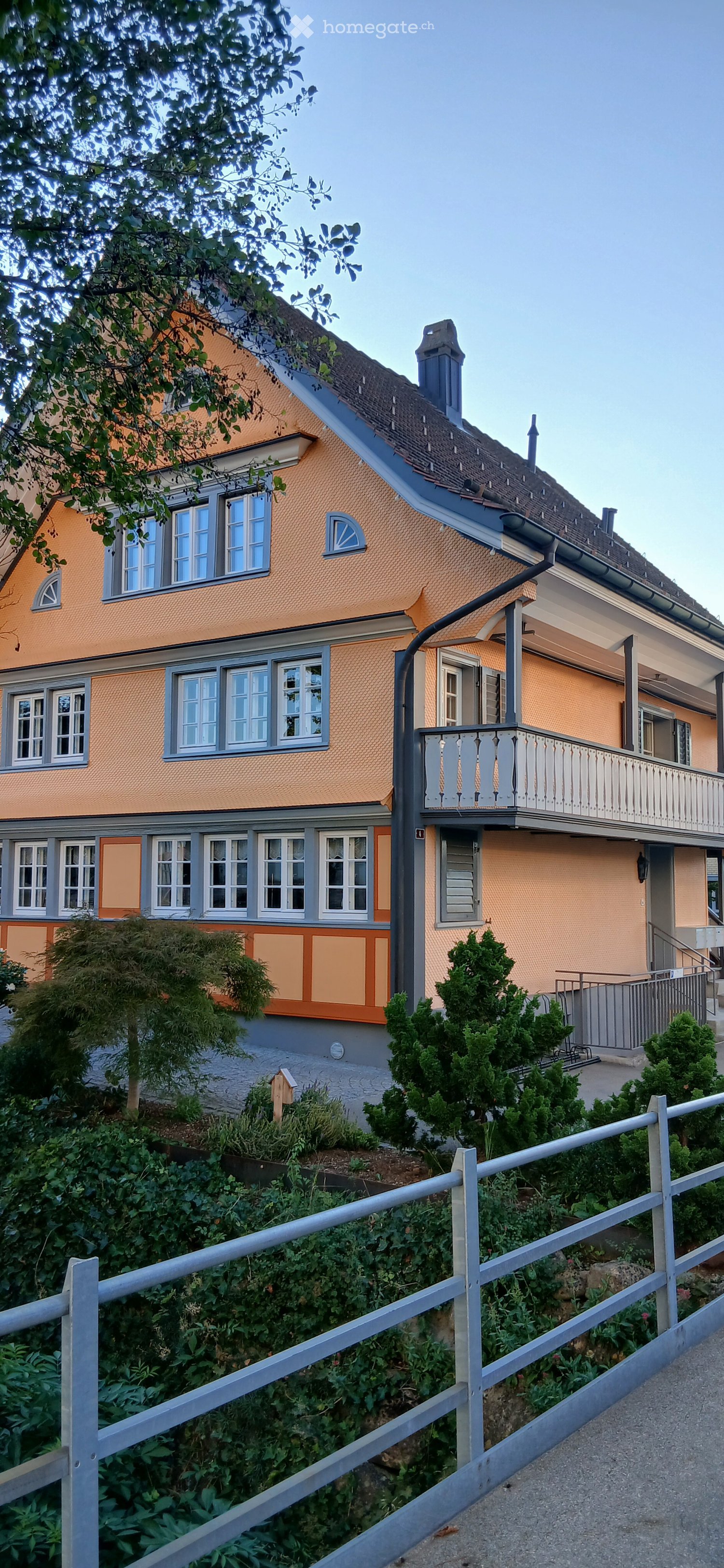 Two-story house with orange and grey exterior, multiple windows, and a balcony on the upper level.