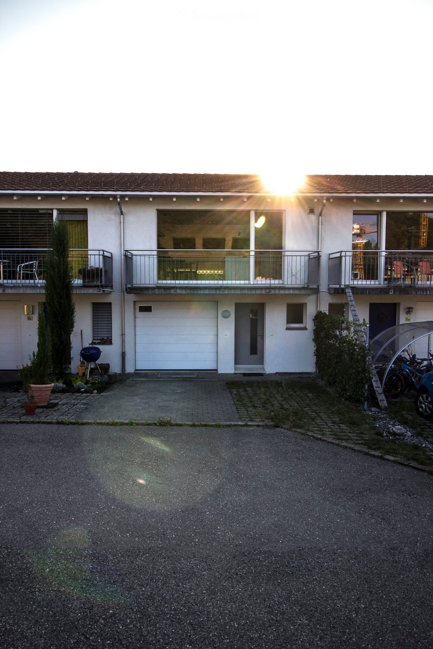 Two-story house with white exterior, multiple windows, balconies, garage, and small garden area.