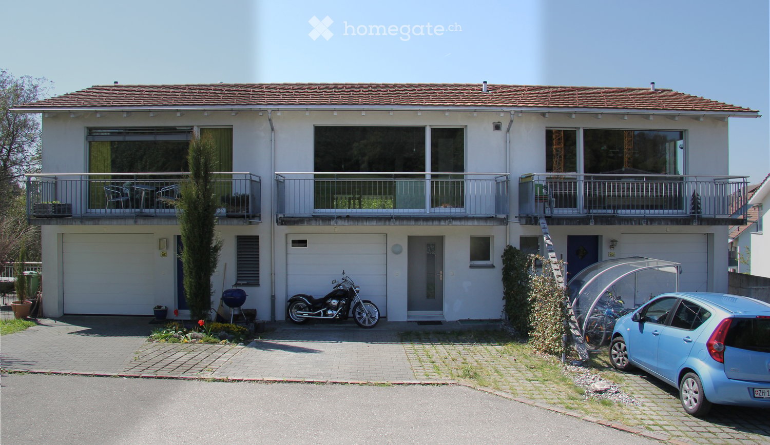 Two-story house with white exterior, tiled roof, multiple balconies, garage, and parking area with a car and motorcycle.