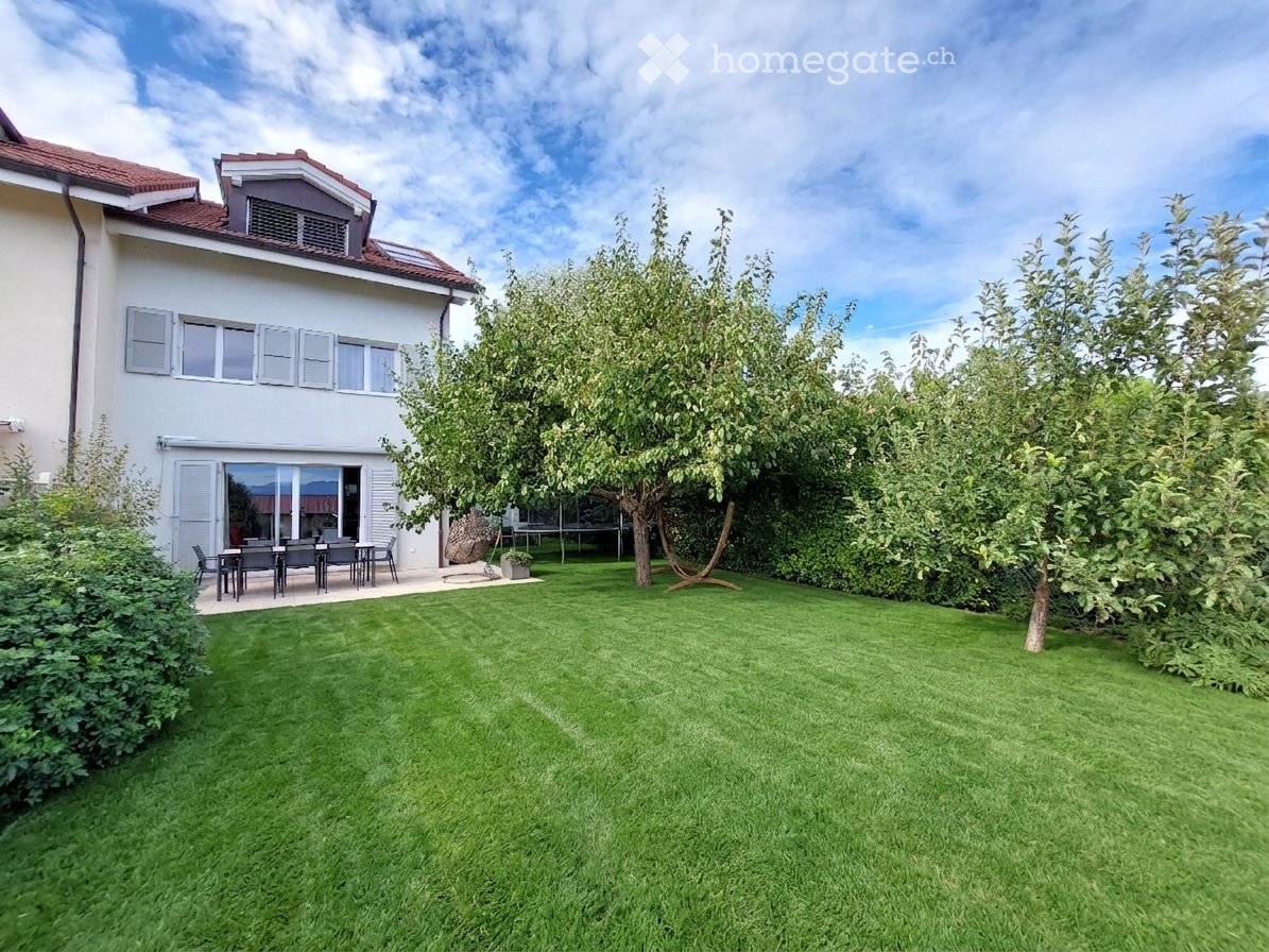 Well-maintained garden with a neatly trimmed lawn, several trees, and a patio area with outdoor furniture near the house.