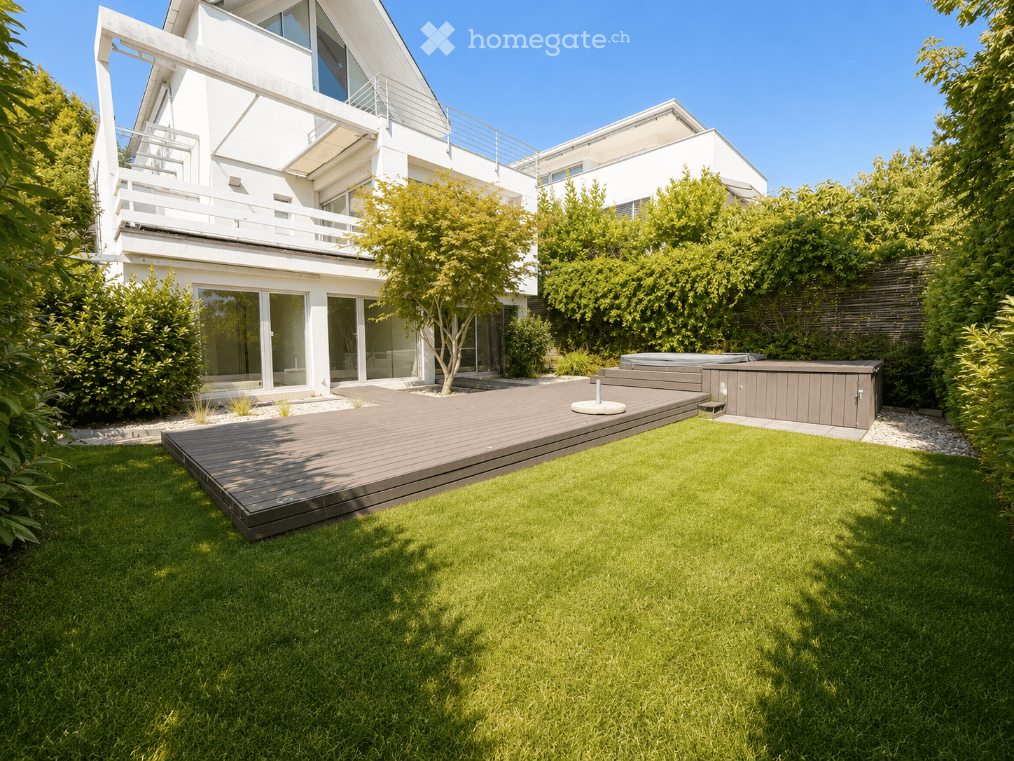 Modern house with a well-maintained garden, featuring a wooden deck, lawn, and a small hot tub area.
