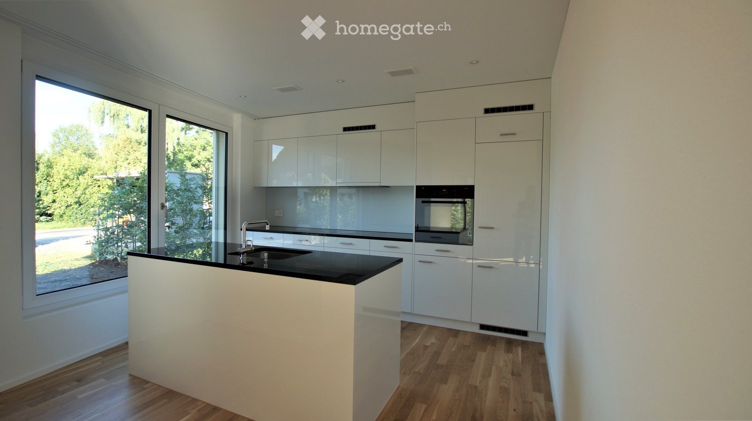 Modern kitchen with white cabinets, black countertop, and a central island. Features a large window with a view of greenery outside.