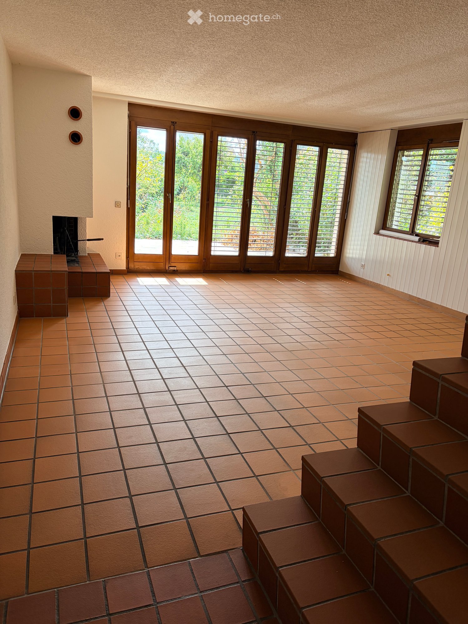 Spacious room with tiled floor, large glass doors leading outside, built-in bench seating, and a fireplace.