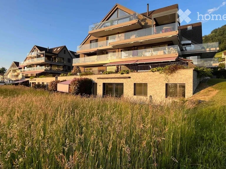 Modern multi-story house, glass balconies, brick ground floor, surrounded by tall grass