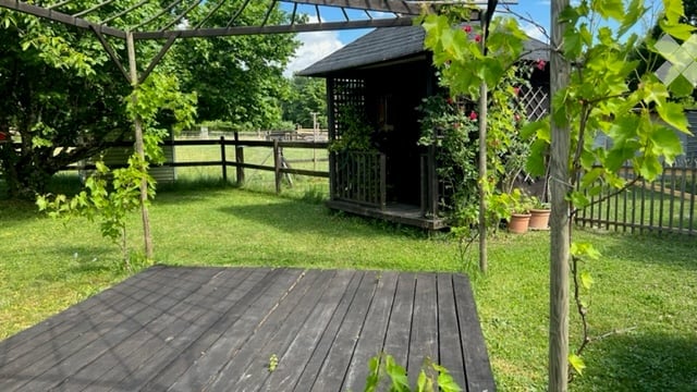 A serene garden area with a wooden deck, lush green grass, and a small gazebo surrounded by climbing plants and potted flowers.