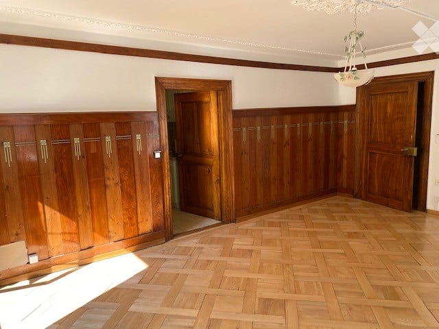 Empty room with wooden panel walls, wooden floor, and two wooden doors.