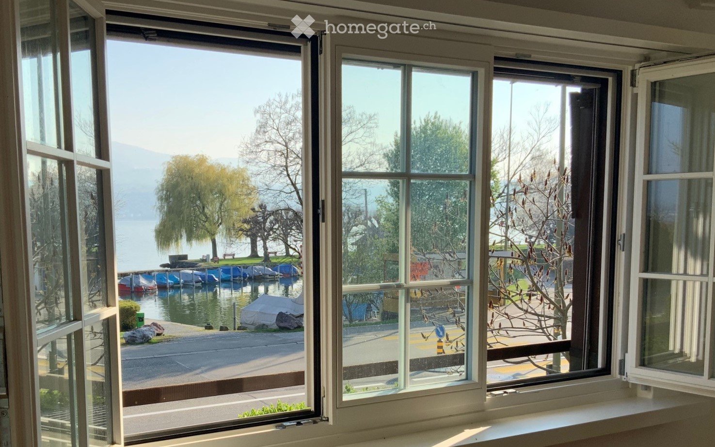 View from a room with large windows overlooking a lake, trees, and docked boats.