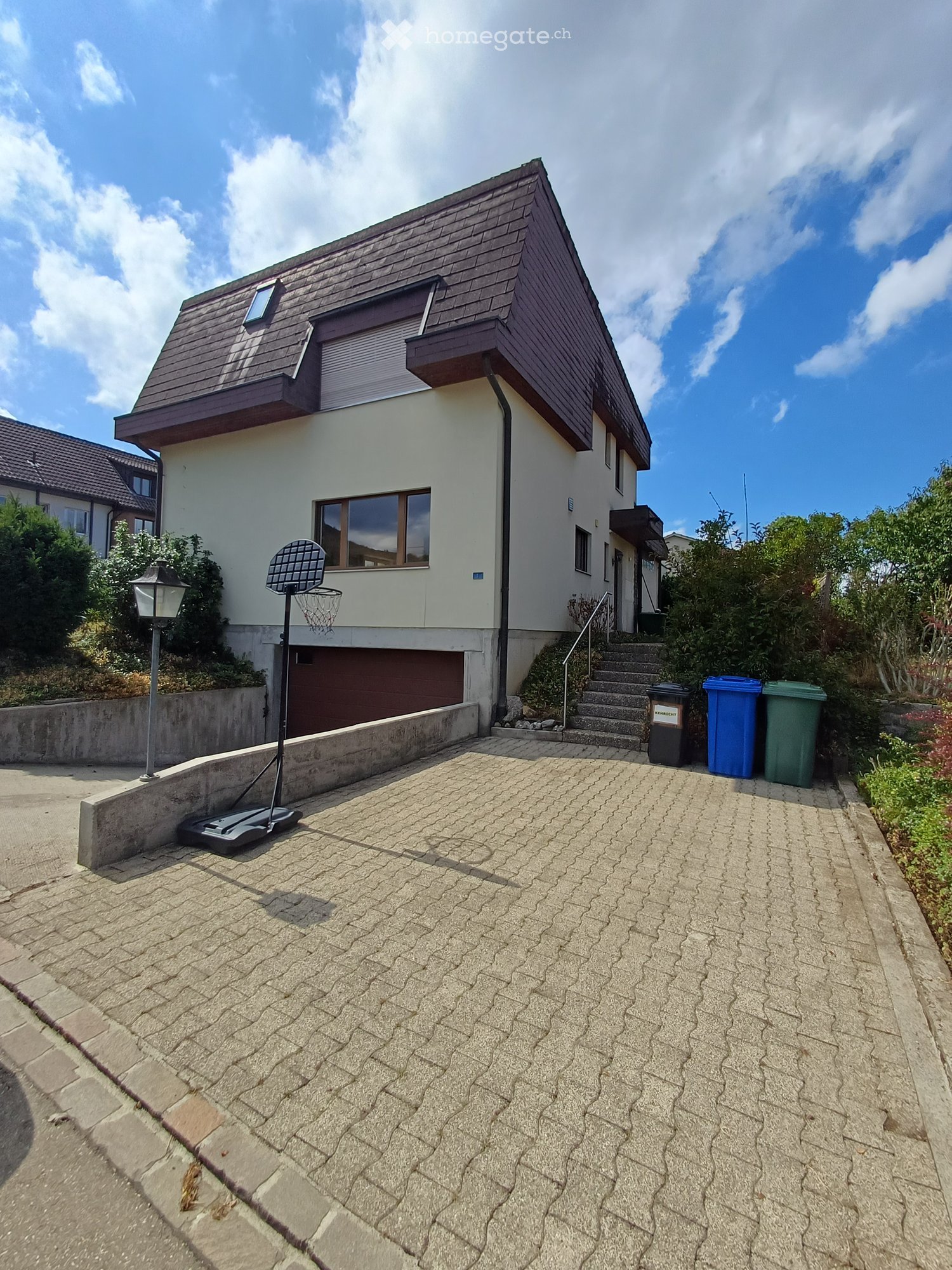 Two-story house with a modern design, featuring a garage, a staircase leading to the entrance, and a small basketball hoop in the driveway.