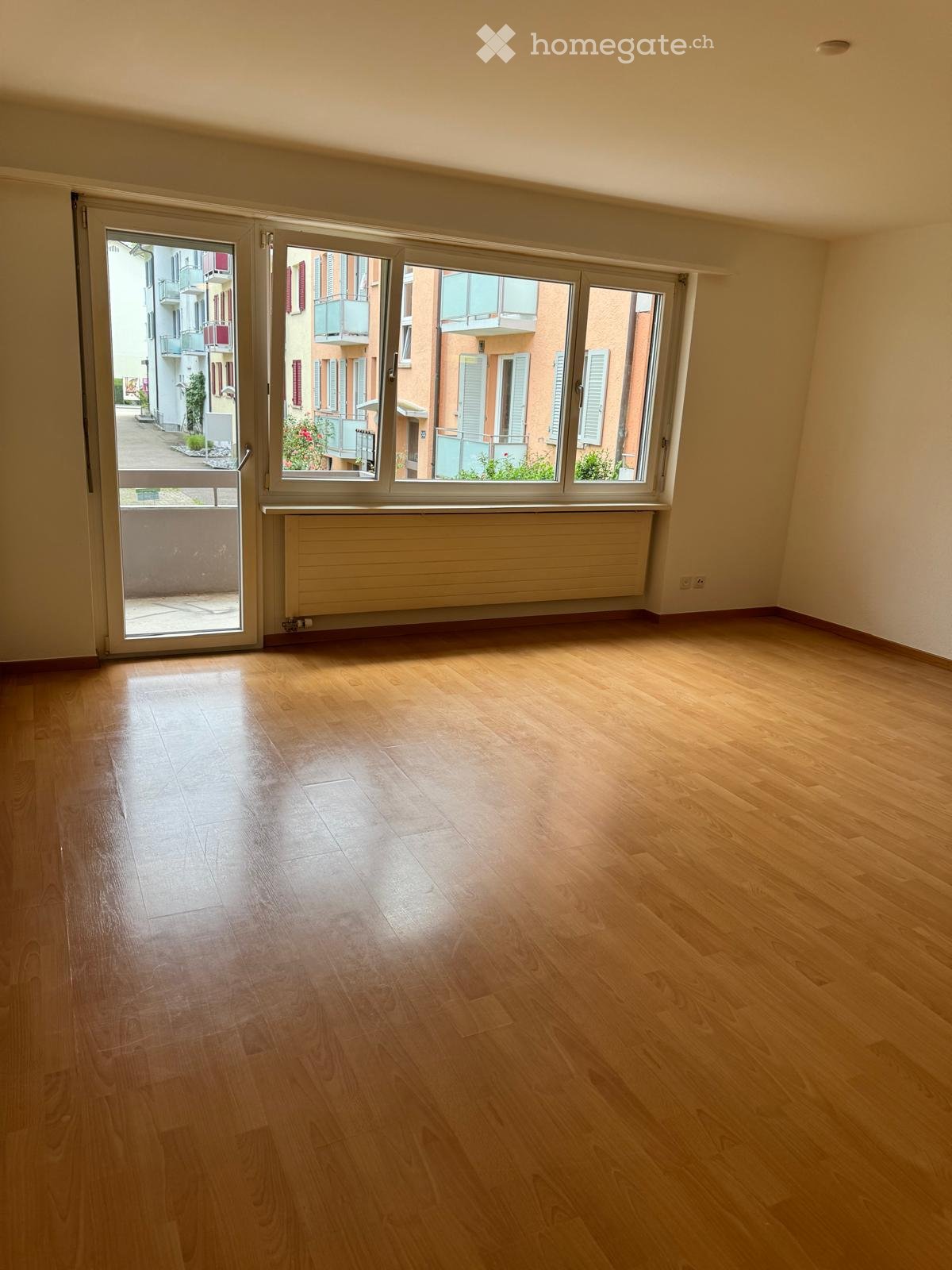 Empty room with wooden flooring, large windows, and a sliding glass door leading to a balcony.