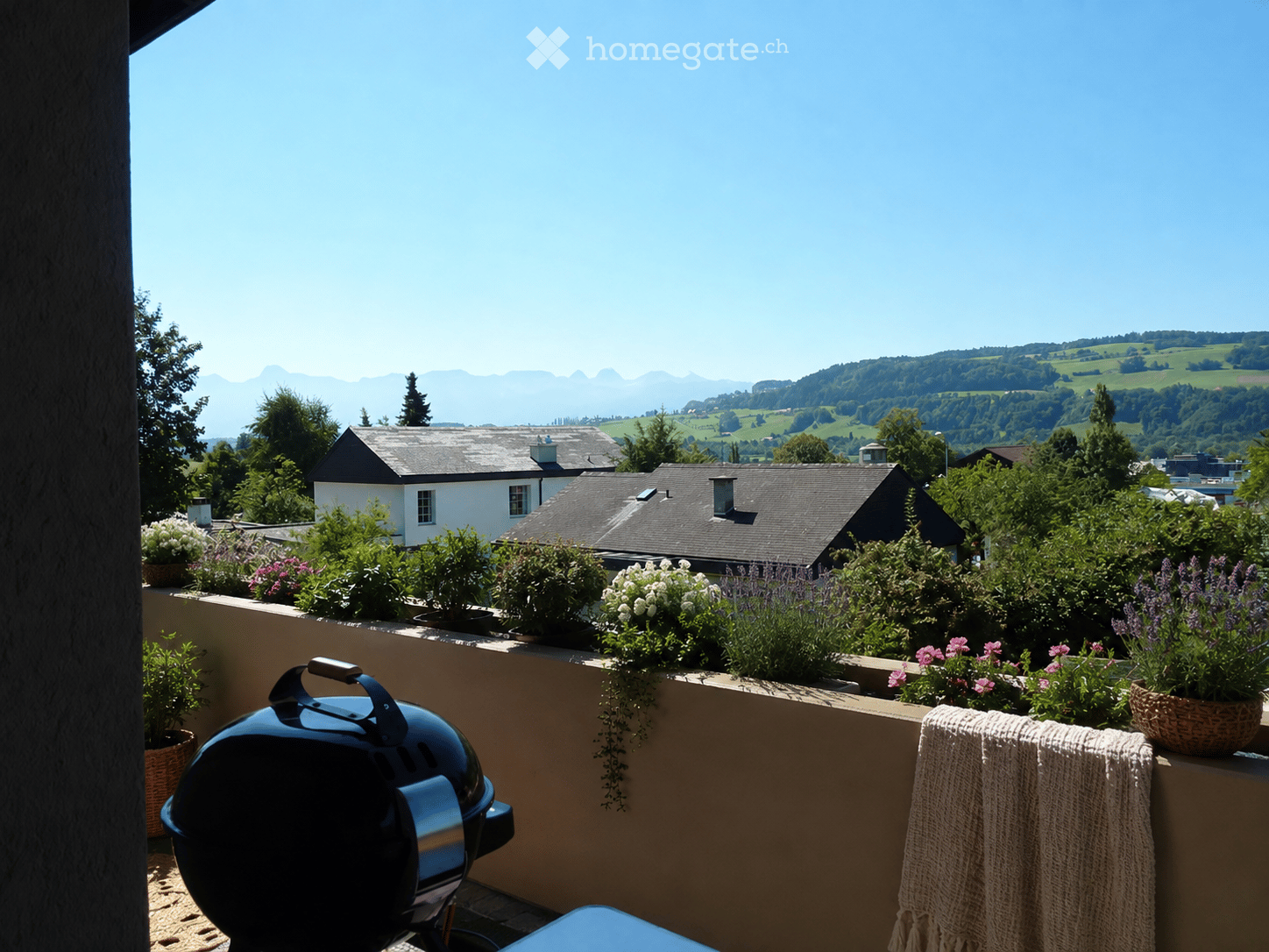 Balcony with a scenic mountain view, featuring a grill, potted plants, and a woven basket with a towel.