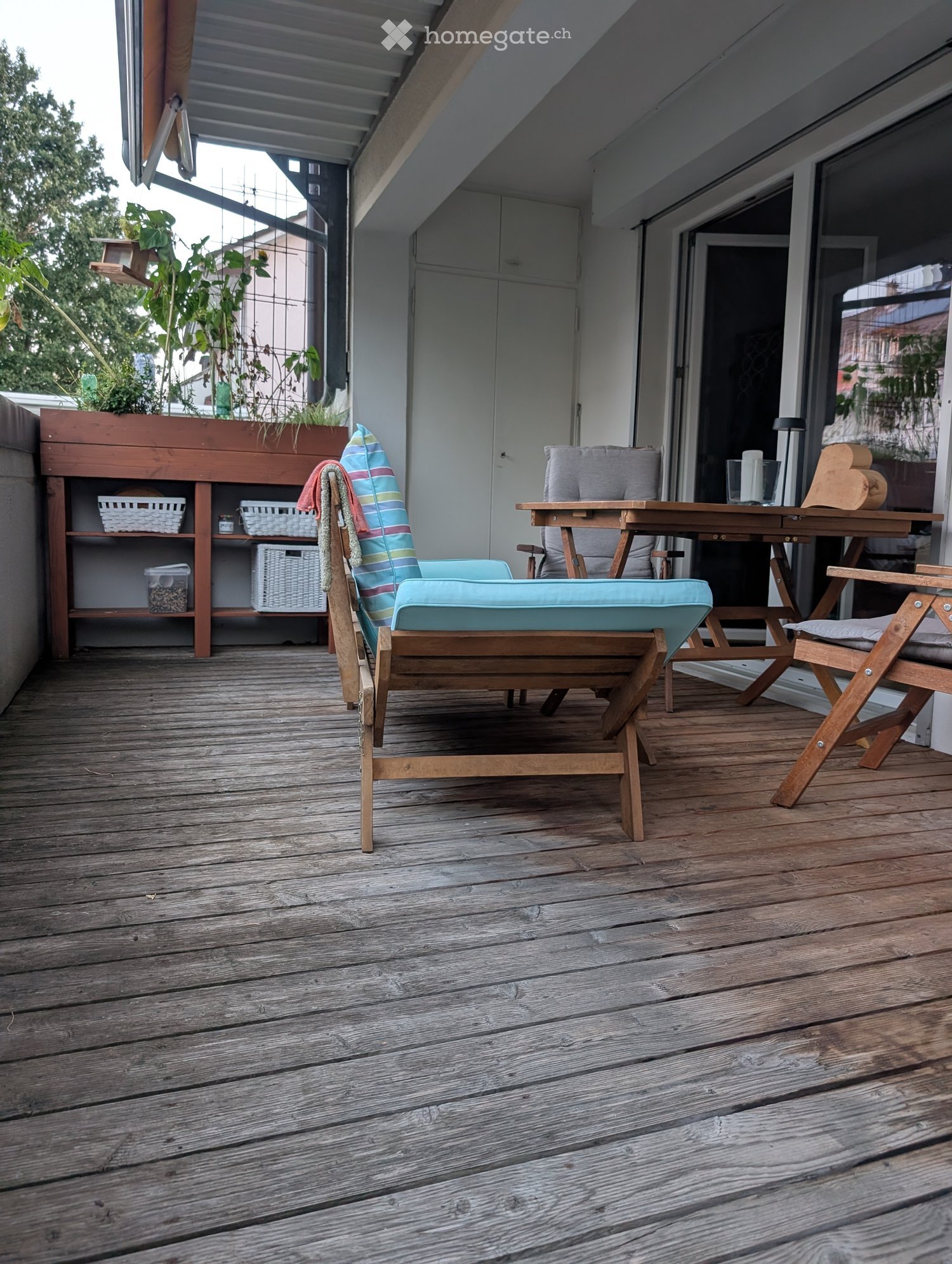 Wooden deck with a lounge chair, small table, shelf with baskets, and a plant box.