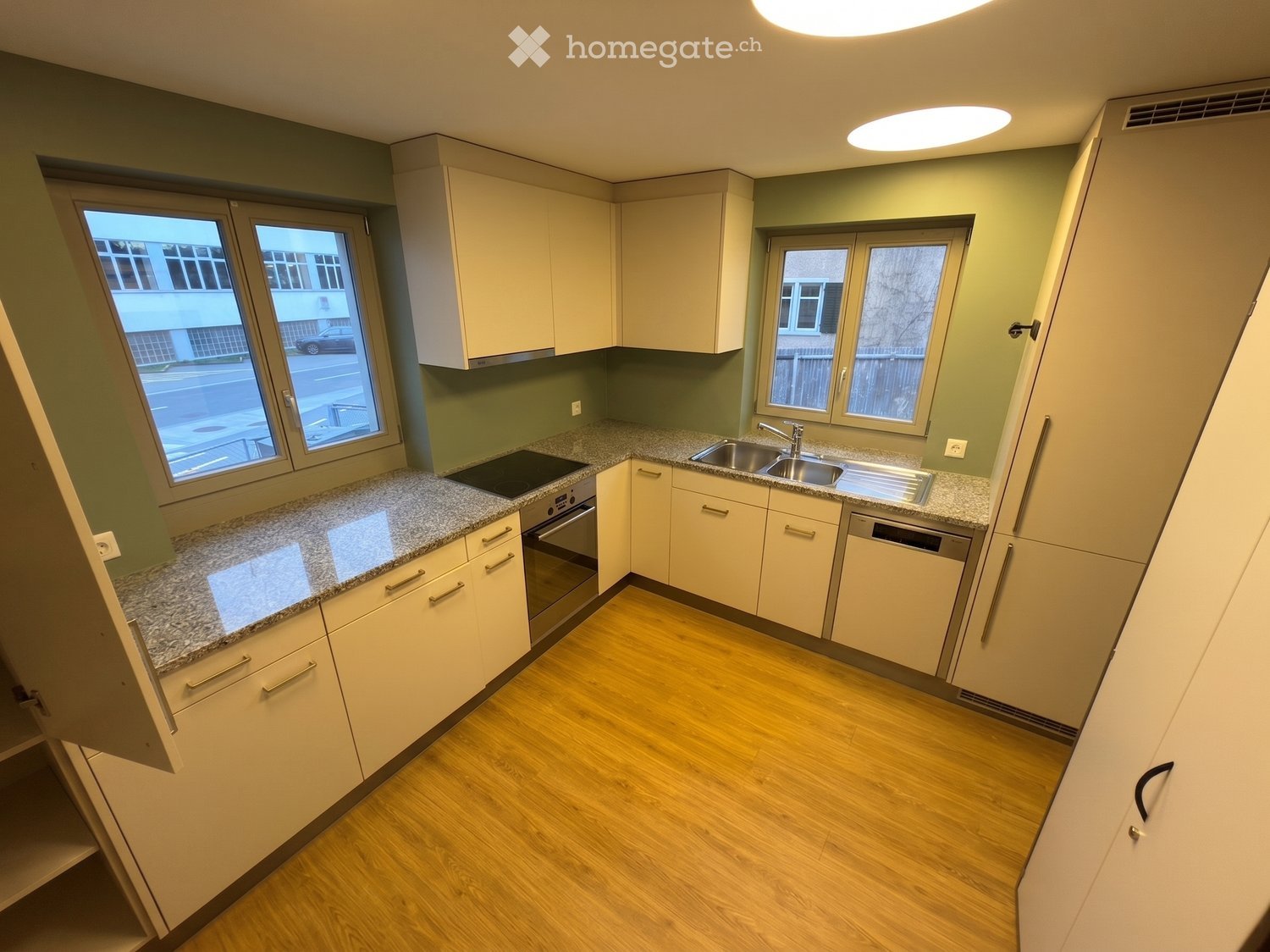 Modern kitchen with light-colored cabinets, granite countertops, and wooden flooring. Features a sink, oven, and dishwasher.