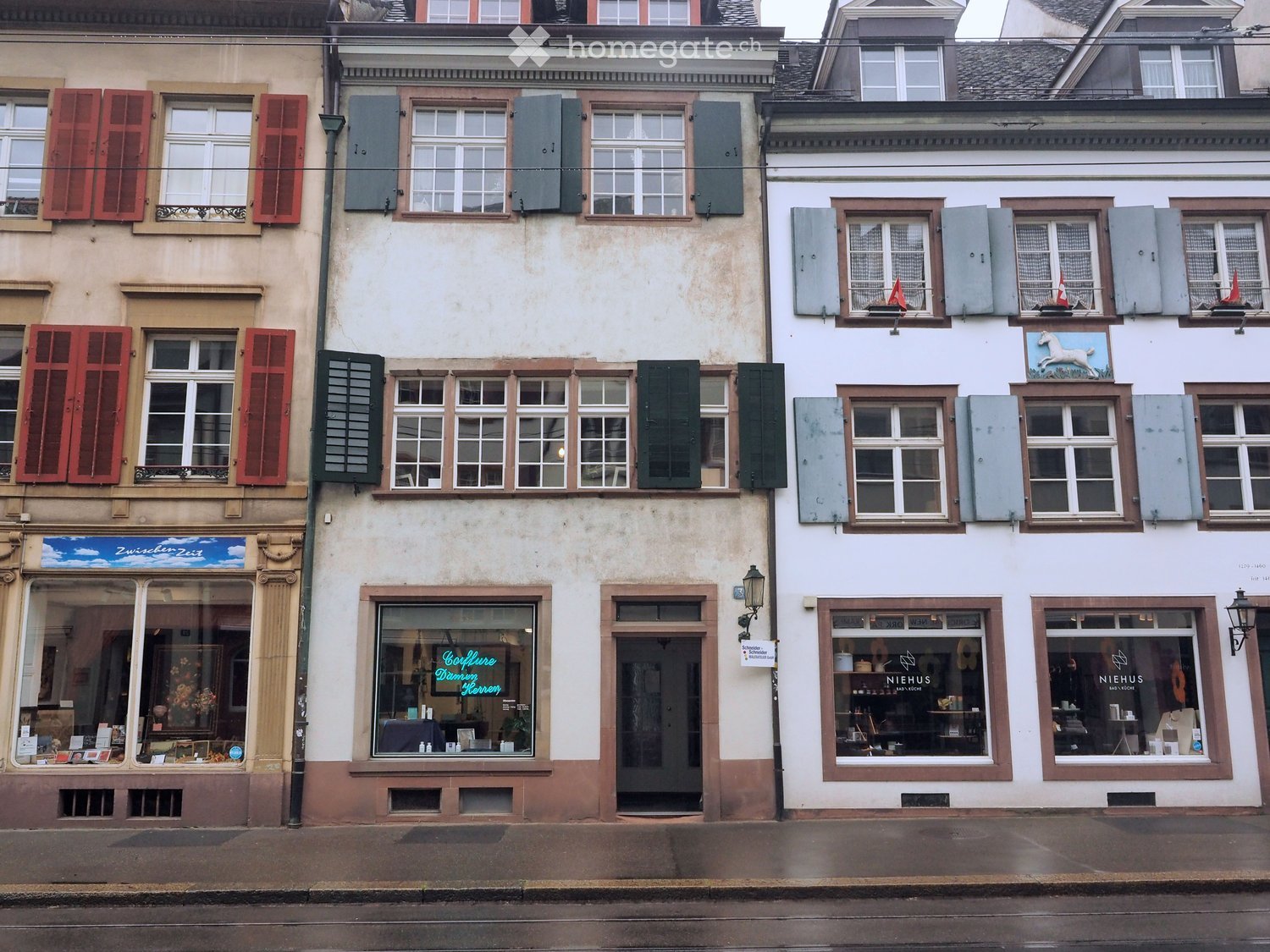 Three-story building with multiple shops on the ground floor, featuring large windows, shutters, and signage for businesses like "Schöder" and "NIEHUS".
