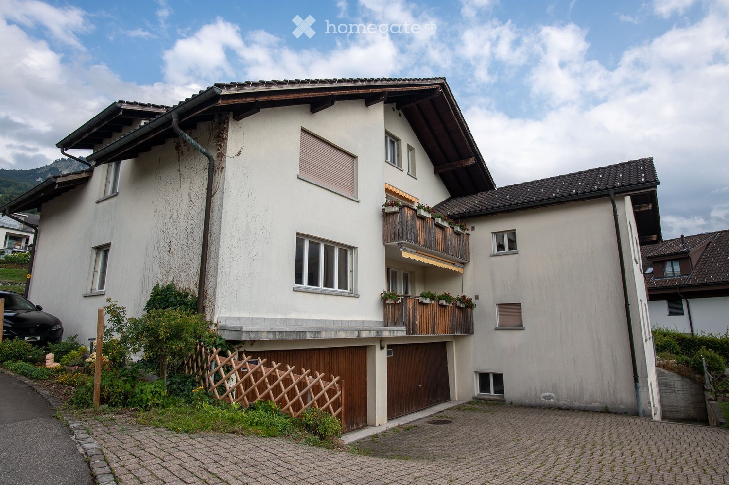 Two-story house with white exterior, wooden balcony, garage, and garden area.
