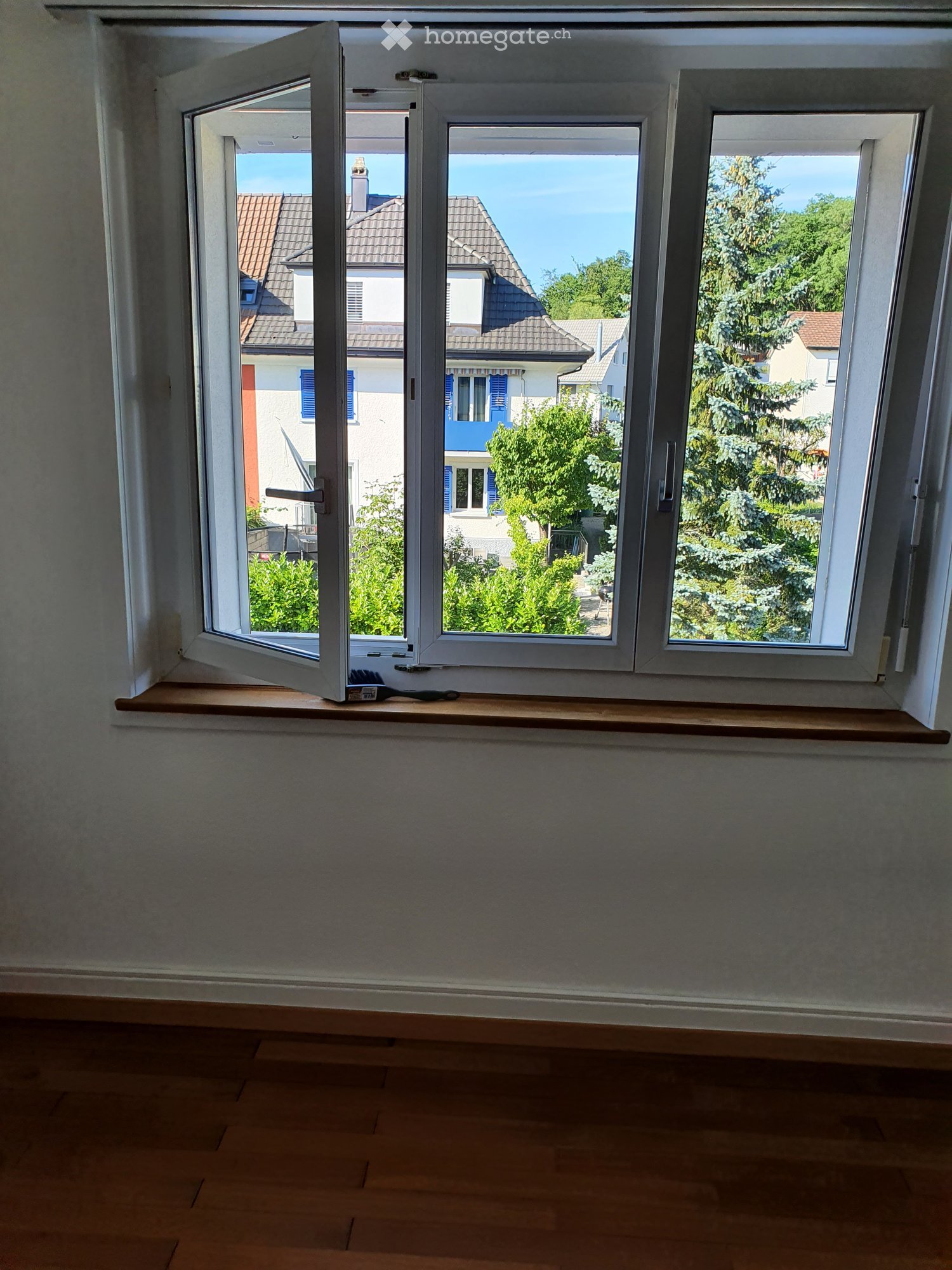 Empty room with wooden flooring, white walls, and a large window with a wooden sill. A small brush is placed on the sill.