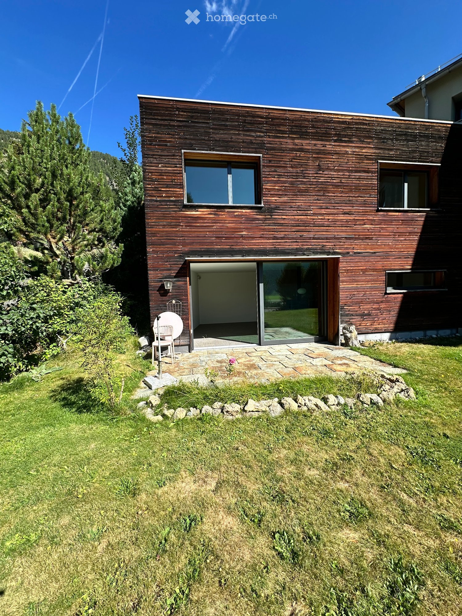 Modern wooden house with large windows and a spacious entrance, surrounded by a well-maintained lawn and trees.