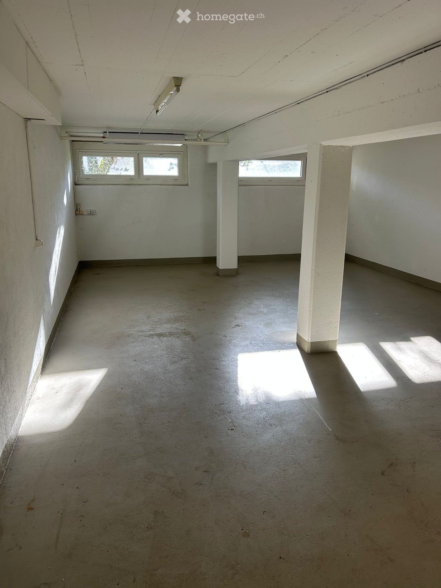 Empty room with concrete floor, white walls, and two windows allowing natural light. No furniture or equipment present.