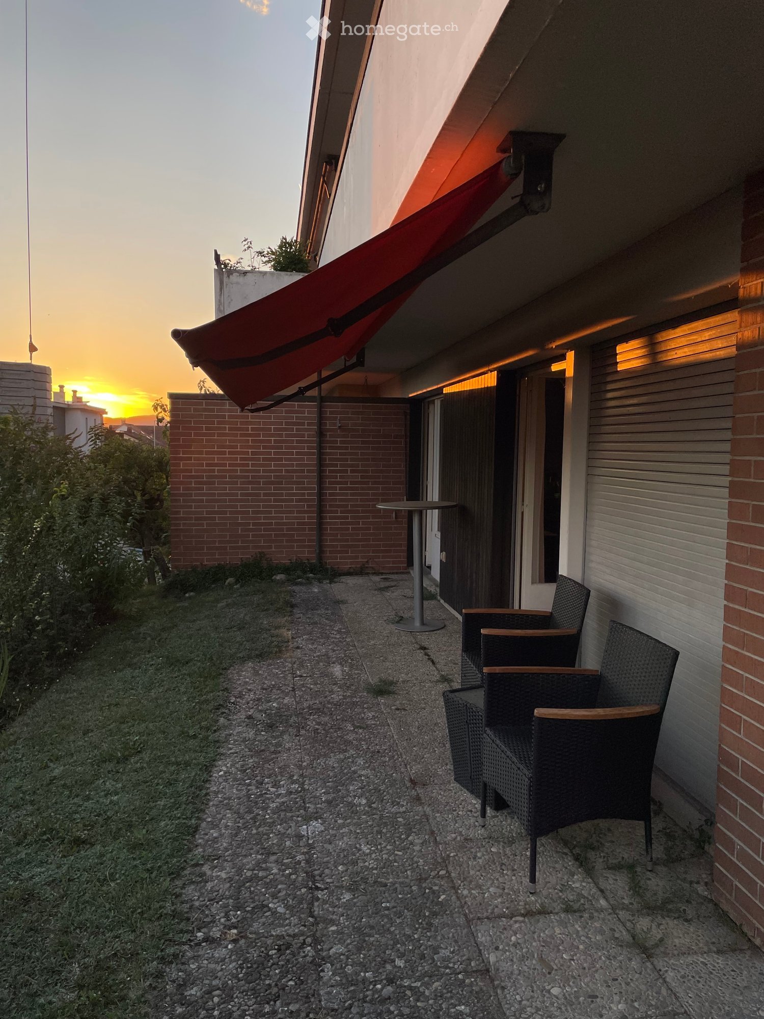 Balcony with a red awning, two wicker chairs, and a small round table.