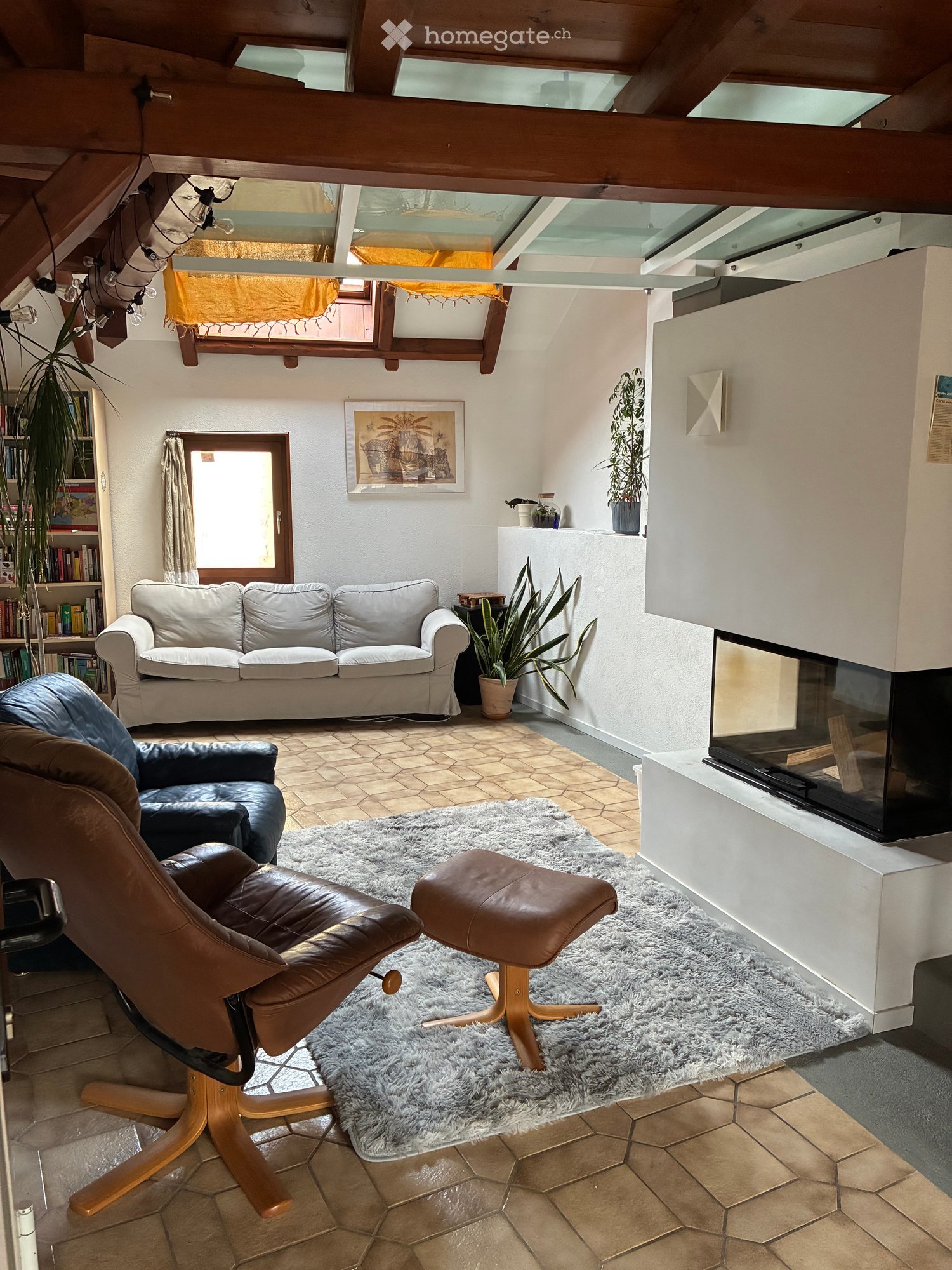 Living room with a white sofa, leather chair, ottoman, fireplace, bookshelf, and plants.