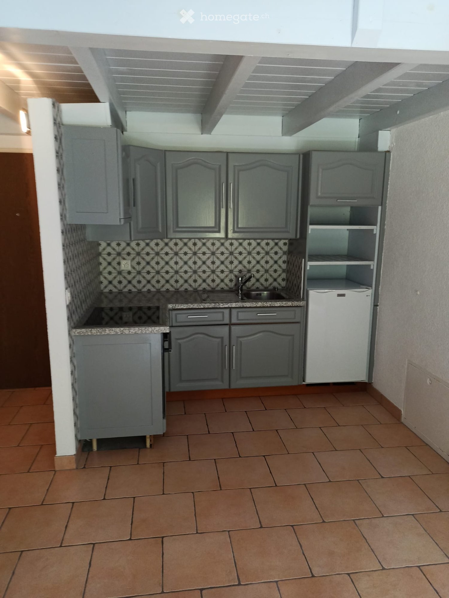 Modern kitchen with grey cabinets, granite countertop, sink, and dishwasher. Brown tiled floor and patterned backsplash.