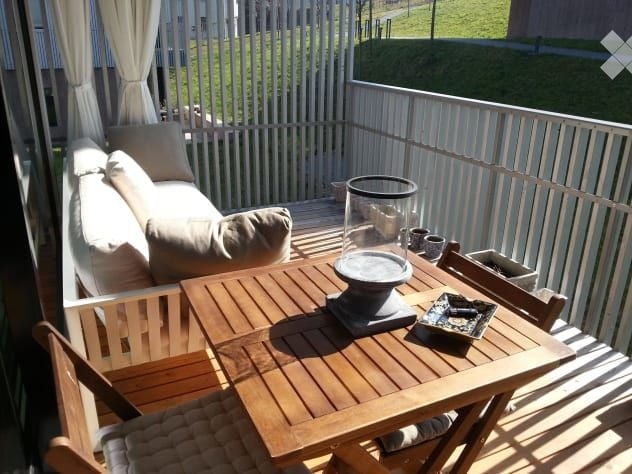 Balcony with wooden table, chairs, sofa, and decorative items.