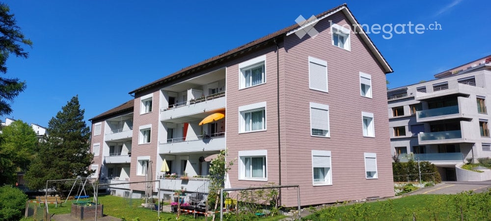 A multi-story residential building with pink siding and white-framed windows, featuring balconies and outdoor seating areas.