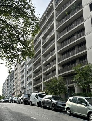 Multi-story residential building with numerous balconies and parked cars along the street.