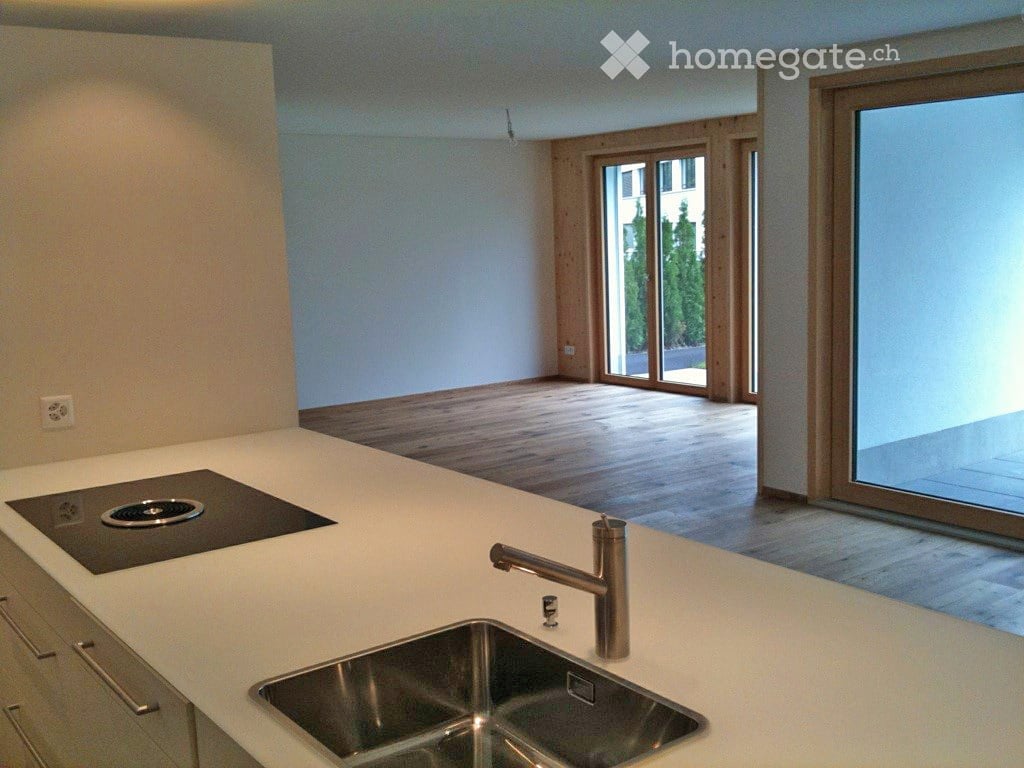 Modern kitchen with white countertops, stainless steel sink, induction cooktop, and large windows offering a view of the outdoors.