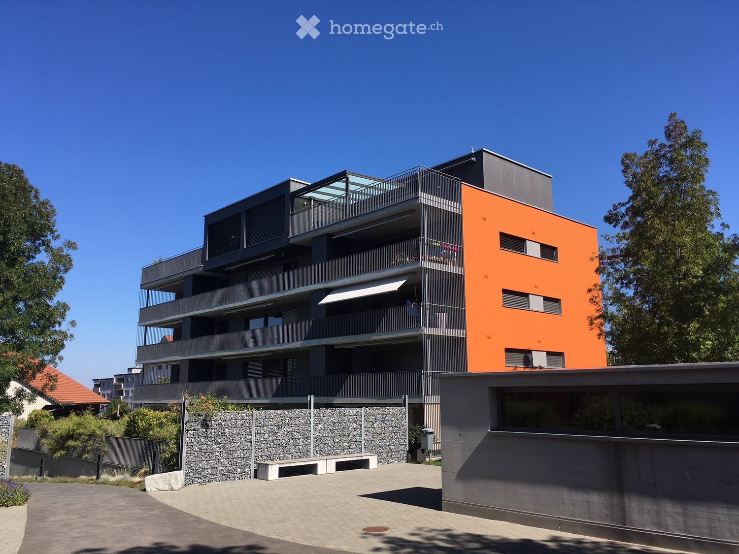 Modern multi-story residential building with orange and grey facade, balconies, and contemporary design.