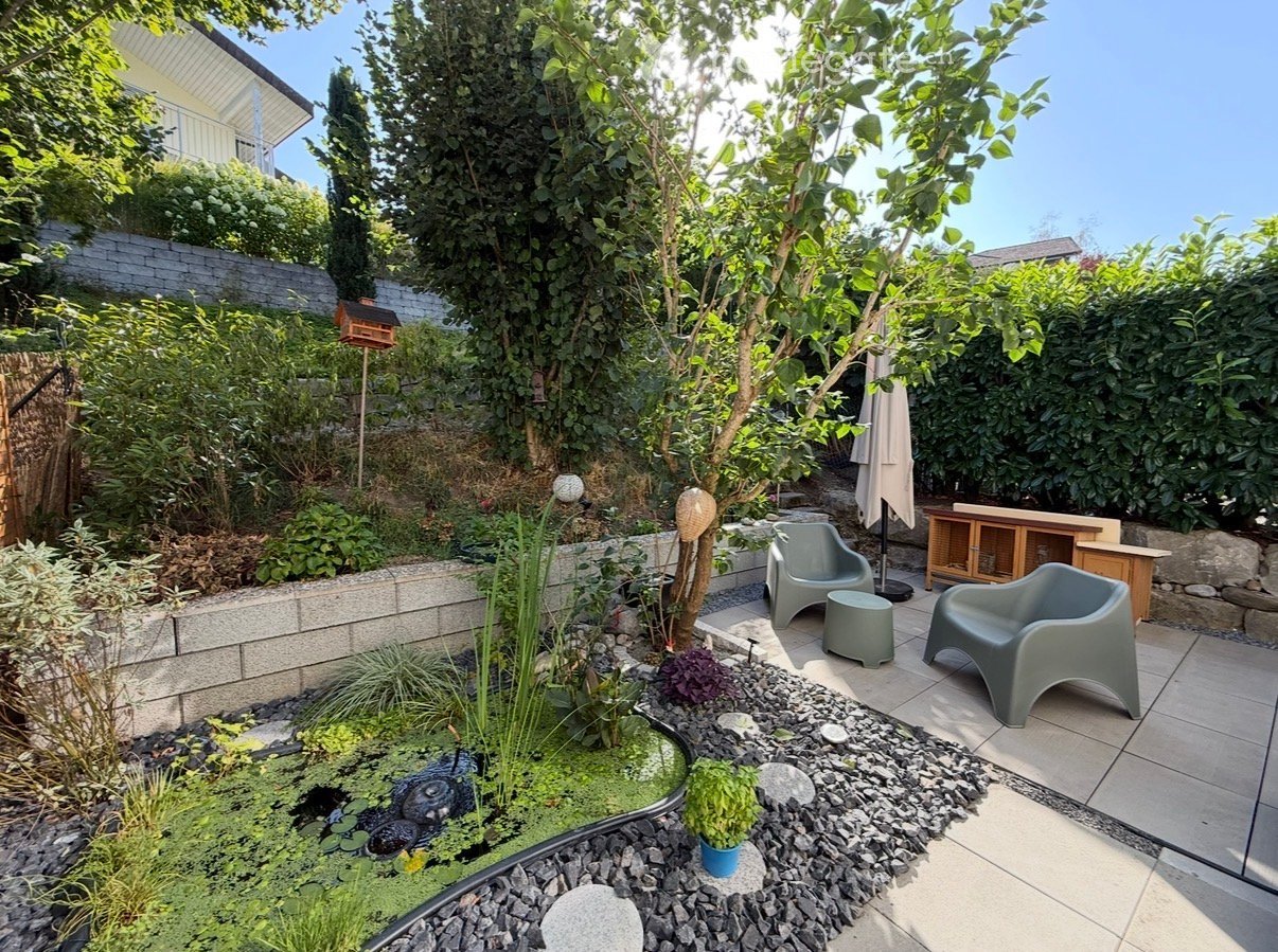Well-maintained garden with a small pond, various plants, a birdhouse, and seating area with chairs and a small table.