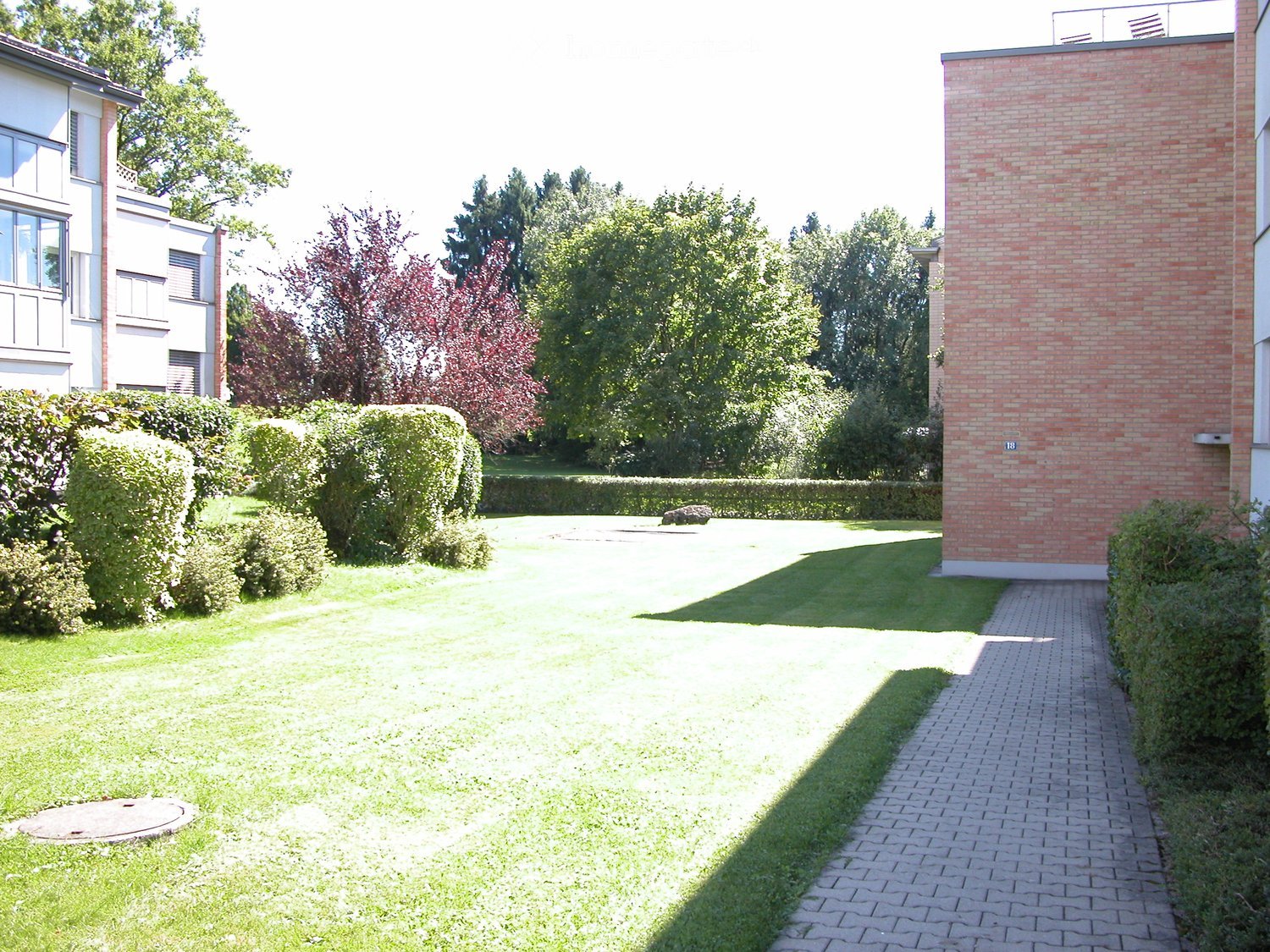 Well-maintained garden with a brick pathway leading to a house entrance, surrounded by neatly trimmed hedges and trees.