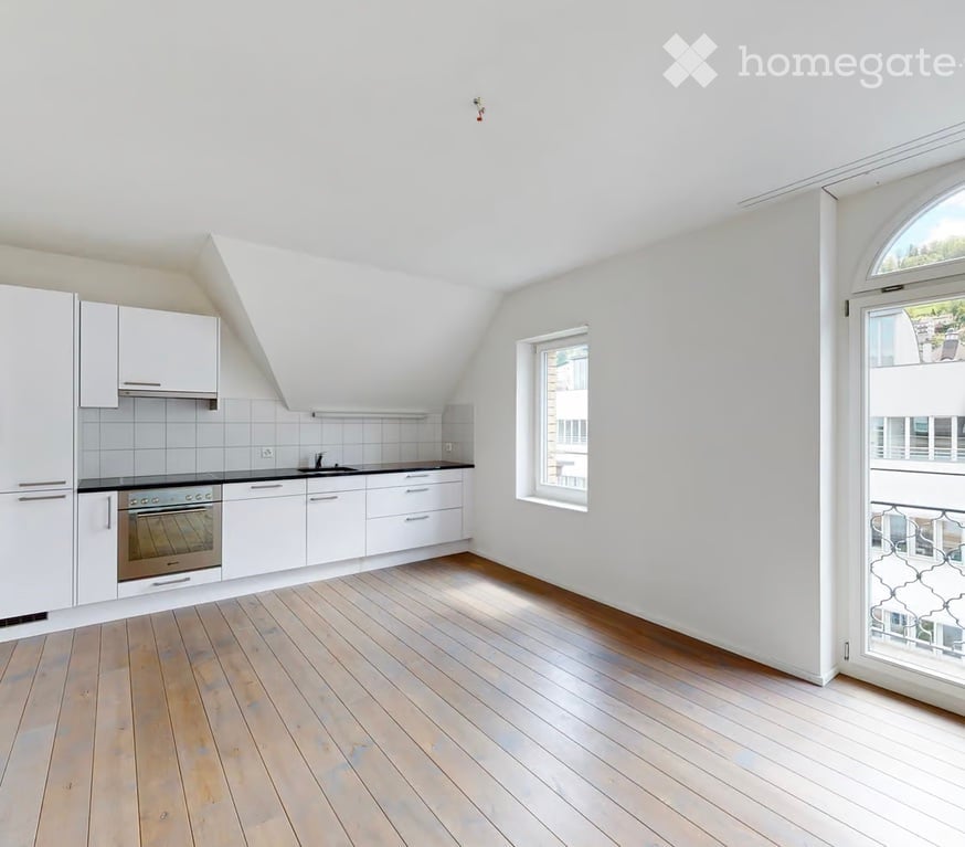 Bright, modern kitchen with white cabinets, stainless steel oven, and wooden flooring. Features a large window and a door leading to a balcony.