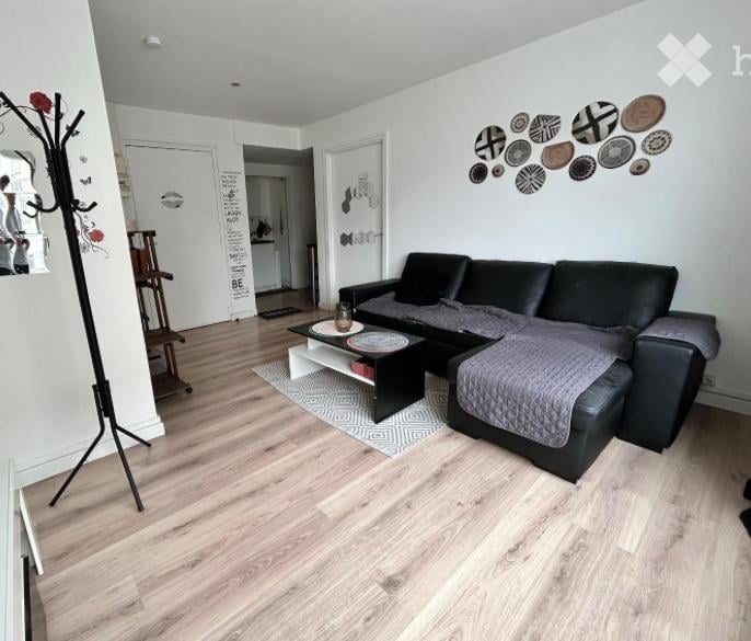 Modern living room with light wooden flooring, black sectional sofa, coffee table, decorative rug, and wall art featuring circular designs.