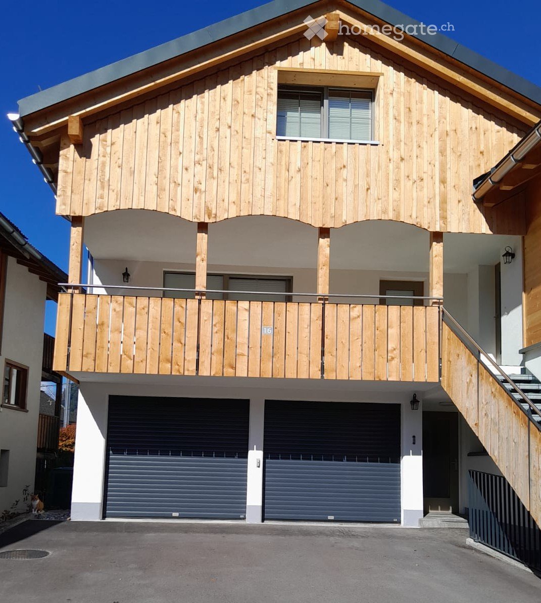 Two-story wooden house with a balcony, garage, and modern design.