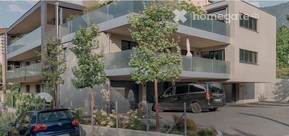 Modern multi-story apartment building with balconies, garage, and parking area.