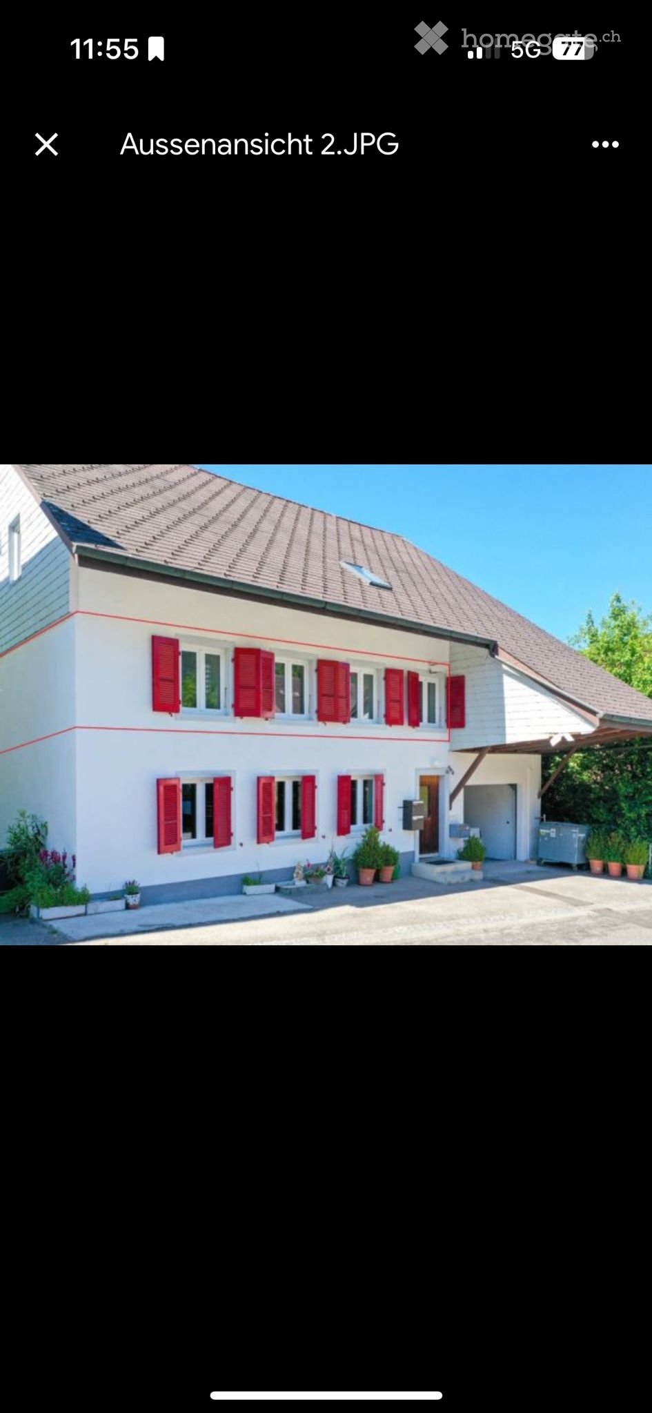Two-story house with white exterior, red shutters, multiple windows, and a small garden area with potted plants.